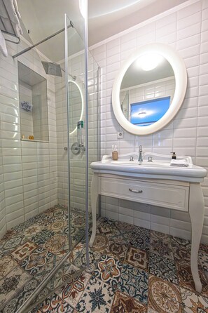 A bathroom with a shower, a sink with a mirror, and patterned floor tiles. - Sigacik Gardenya Boutique Hotel (Seferihisar)