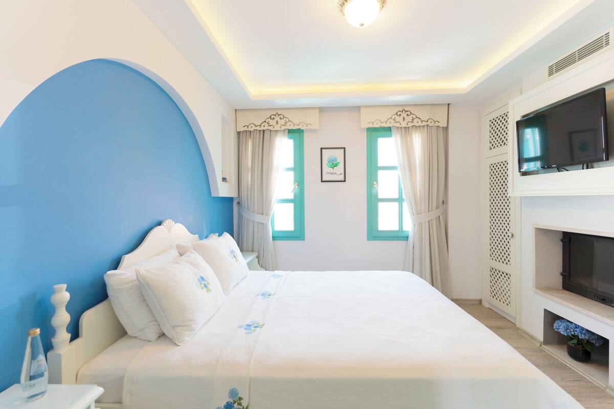 Un dormitorio con una cama grande, televisión y chimenea.