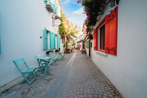 A narrow cobblestone street with turquoise chairs and tables, white walls, and red shutters. - Sigacik Gardenya Boutique Hotel (Seferihisar)