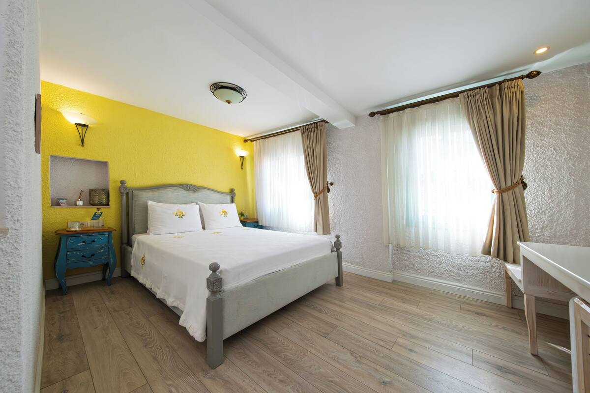 Un dormitorio con cama, mesita de noche, lámpara y cortinas.