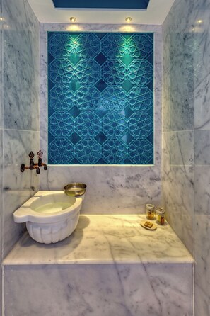 Une salle de bain avec un bidet en céramique blanche, un mur décoratif recouvert de carreaux bleus et un sol en marbre.