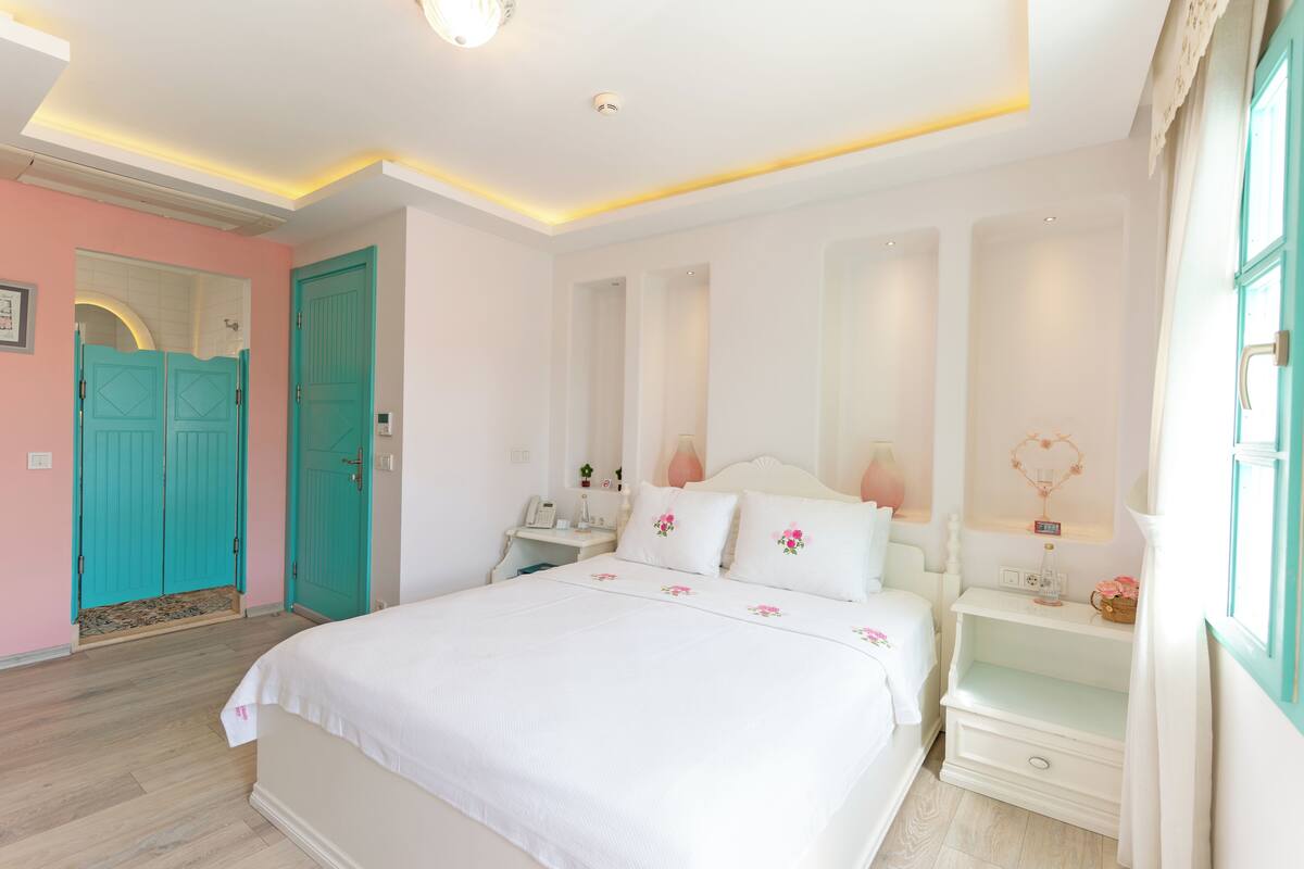 Un dormitorio con una cama grande, una mesita de noche, un aparador y una ventana con cortinas.