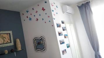Een kamer met een blauwe wand, een decoratieve spiegel, vlinderstickers op de muur en een reeks ingelijste foto's.