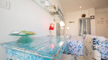 Una habitación con una mesa azul, una lámpara roja y una cama con edredón estampado.