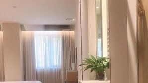 Une chambre d’hôtel avec deux lits, une petite table avec une plante, un miroir et une fenêtre avec des rideaux.