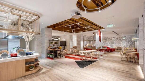 Un restaurant moderne doté d’une salle à manger principale, d’un bar et d’une cuisine visible au fond de la salle.