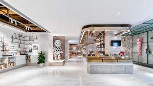 Un hall d’hôtel moderne avec un comptoir d’accueil central, une grande sculpture représentant un dalmatien et un espace bar fermé par des parois de verre.