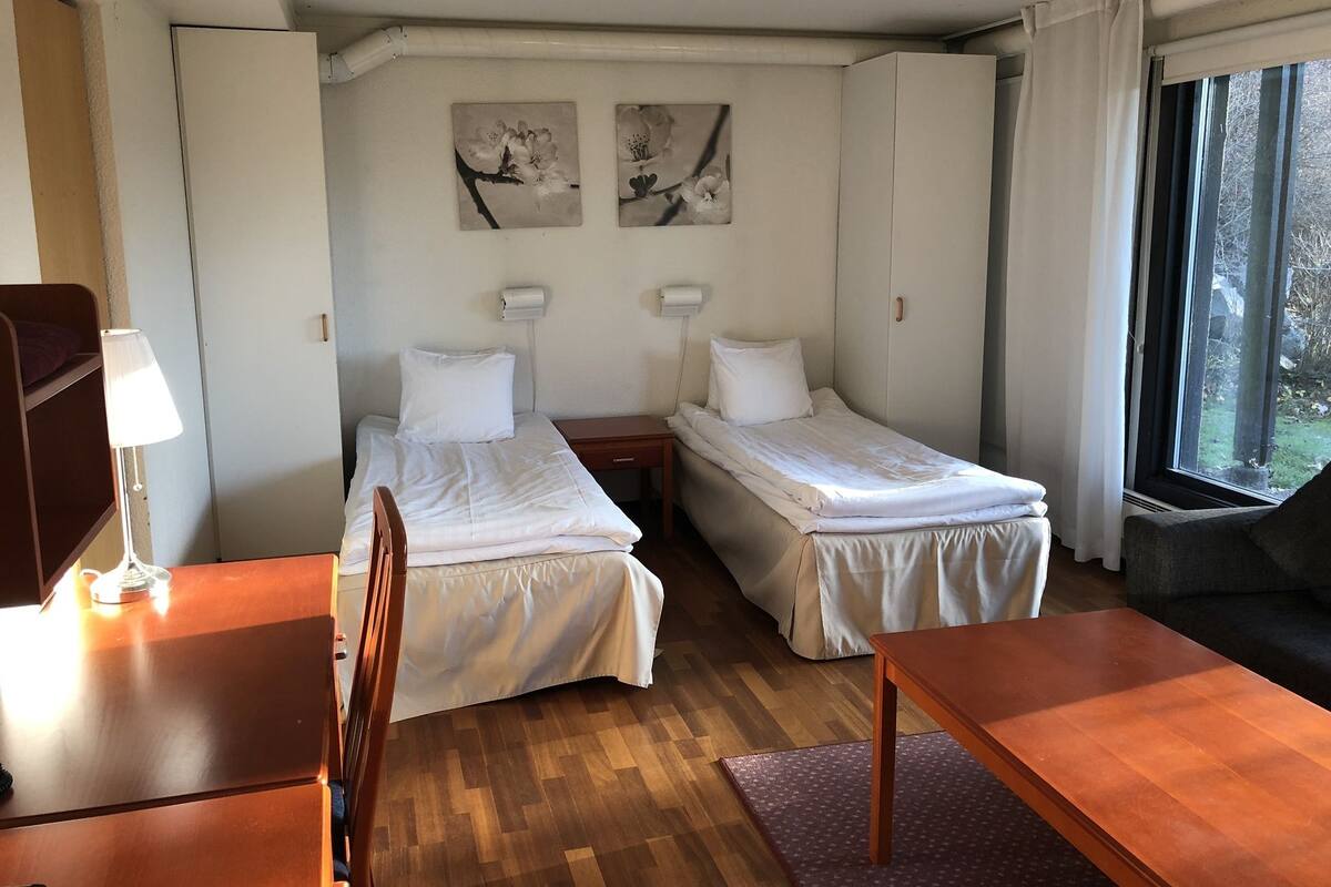 Una habitación con dos camas individuales, un escritorio de madera, una silla, una mesa y una ventana con cortinas.