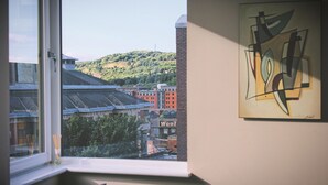 Quarto com janela para uma vista urbana, um quadro abstrato emoldurado e uma placa visível com 'Wool'.