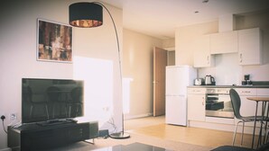 Uma cozinha moderna com armários brancos, geladeira, forno e cafeteira. Há uma área de jantar com mesa e cadeiras.