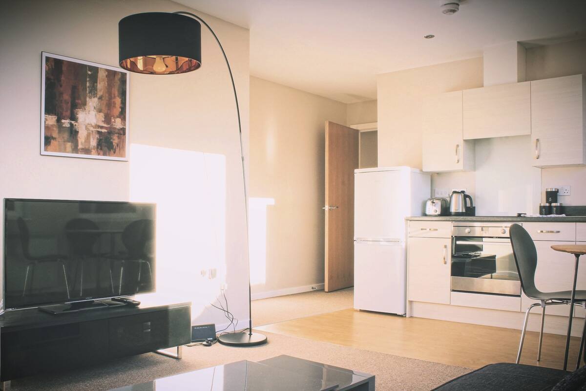 A modern kitchen with white cabinets, a refrigerator, an oven, and a coffee maker. There's a dining area with a table and chairs.