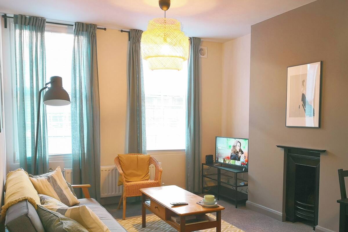 A living room with a sofa, armchair, coffee table, TV, fireplace, and curtains.