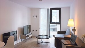A modern living room with a flat-screen TV, a glass coffee table, a laptop, and a dining area with chairs. - Homely Serviced Apartments - Blonk St (Sheffield)