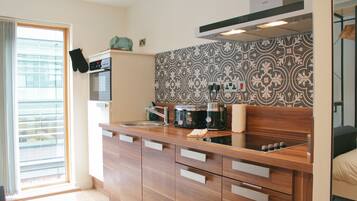 A modern kitchen with a built-in oven, a coffee maker, and a microwave. There is a window with blinds on the left side.