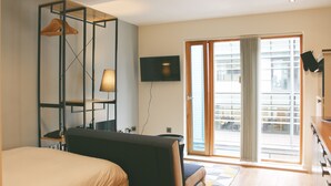 A modern hotel room with a bed, a desk, a TV, and a large sliding glass door to the outside. - Homely Serviced Apartments - Blonk St (Sheffield)