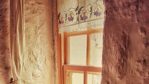 A cozy room with a wooden bench, a small table with cups and a cactus, and a window with a curtain. - Lilyum Alaçatı Butik Otel (Cesme)