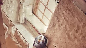 A room with a bed, a small table with decorative items, a window, and a textured wall. - Lilyum Alaçatı Butik Otel (Cesme)