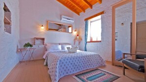A bedroom with a wooden ceiling, a bed with a floral bedspread, a small table with a plant, a mirror, and an air conditioning unit. - Lilyum Alaçatı Butik Otel (Cesme)