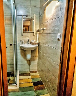 A bathroom with a glass shower enclosure, a sink with toiletries, and a tiled floor with a checkered pattern. - Lilyum Alaçatı Butik Otel (Cesme)