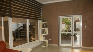 A living room with a large window, a sliding door, and a white coffee table. - Sapphire Court (Accra)