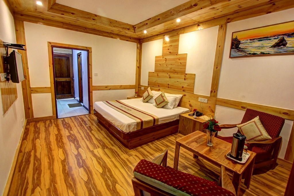 Una habitación con suelo de madera, una cama, una mesita con una tetera y una silla.