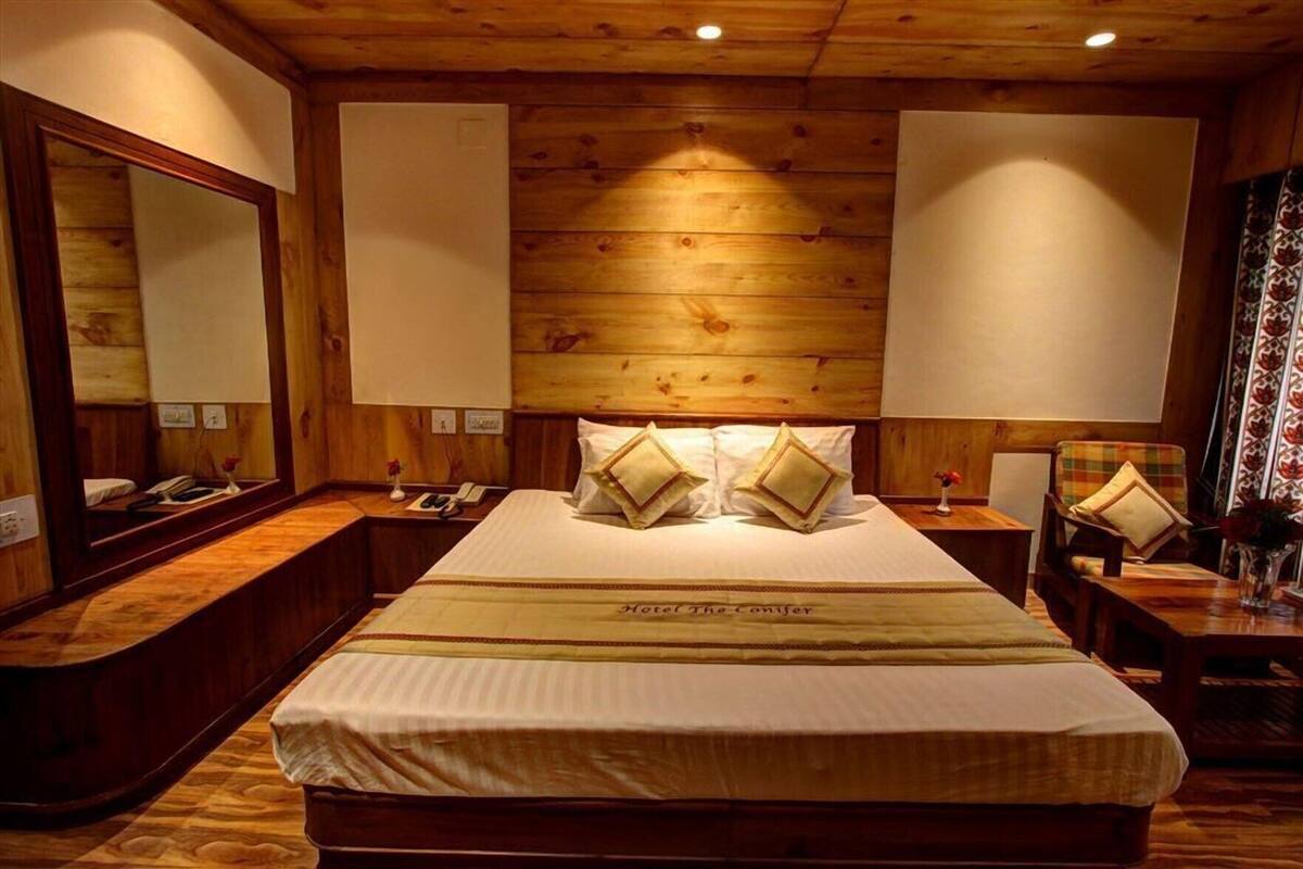 Habitación de hotel con una cama grande, paneles de madera, un espejo, mesitas de noche y una mesita de noche con lámpara.
