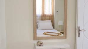 Une chambre à coucher avec un miroir à cadre en bois, un lit recouvert de linge de maison blanc, une table de chevet avec une lampe et un petit objet décoratif posé sur la table de chevet.