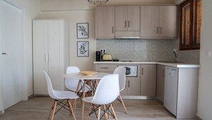 Une cuisine compacte avec des meubles blancs, une table à manger avec des chaises blanches et un petit plan de travail sur lequel se trouvent un grille-pain et une bouilloire.