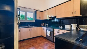 A modern kitchen with wooden cabinets, a black countertop, and a window providing natural light. - Villa Aris (Archaia Olympia)