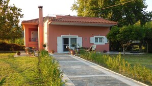 A house with a paved pathway leading to the entrance, surrounded by greenery and potted plants. - Villa Aris (Archaia Olympia)