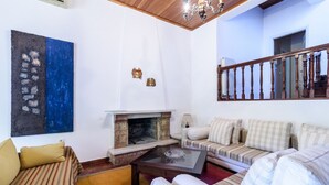 A living room with a fireplace, striped sofa, and a chandelier. - Villa Aris (Archaia Olympia)