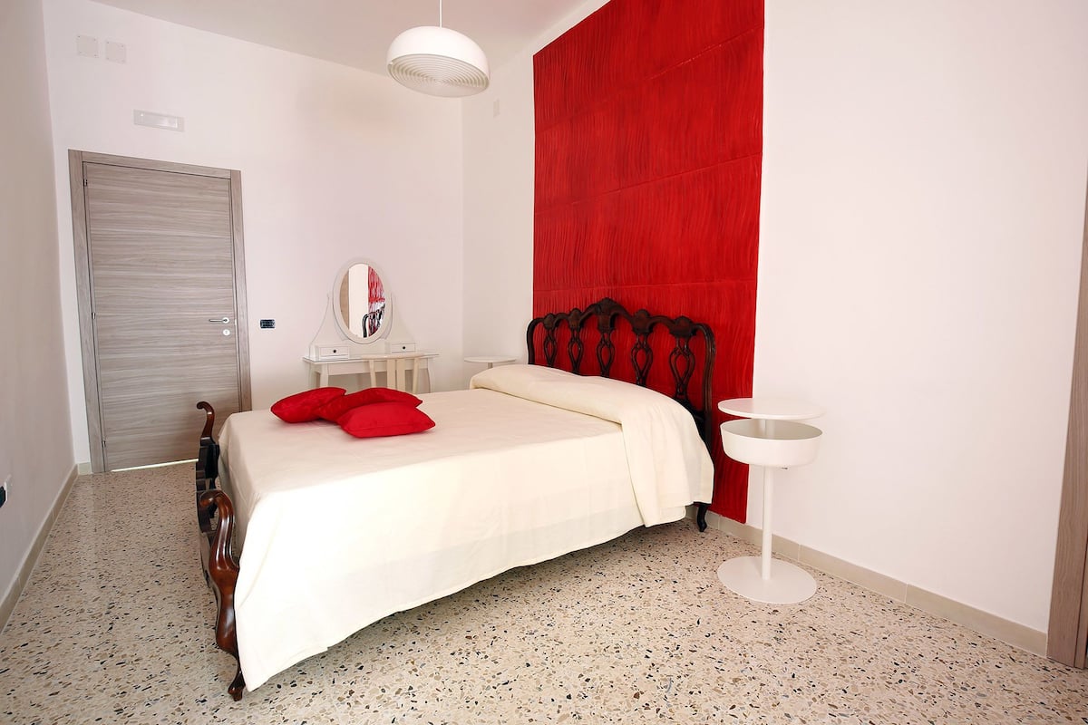 Un dormitorio con cama, pared de acento roja, tocador blanco y una mesa redonda.