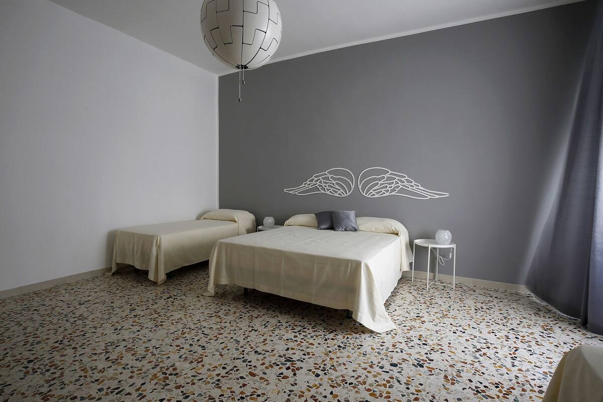 Un dormitorio con dos camas, un candelabro en el techo, un adorno en la pared y una mesita de noche con lámpara.