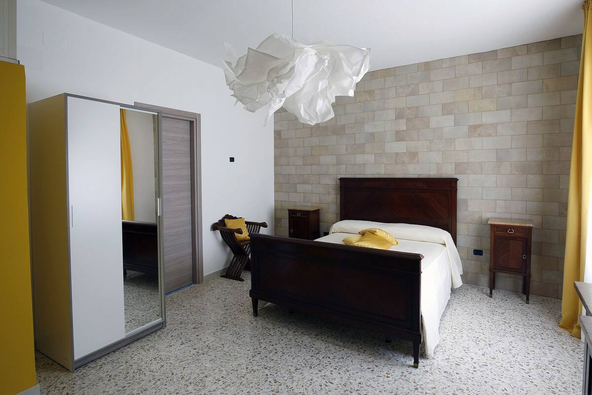 Un dormitorio con una cama, un armario, un espejo y una lámpara colgante.