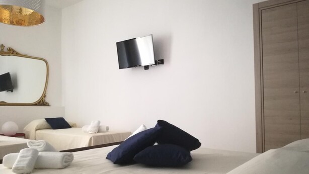 Hotellihuone, jossa on sänky, seinälle asennettu televisio, peili ja vaatekaappi.