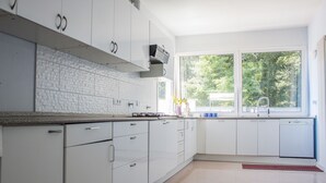 A modern kitchen with white cabinets, a tiled backsplash, and a window providing a view of greenery outside. - Casa Bella Il Castello (Vergato)