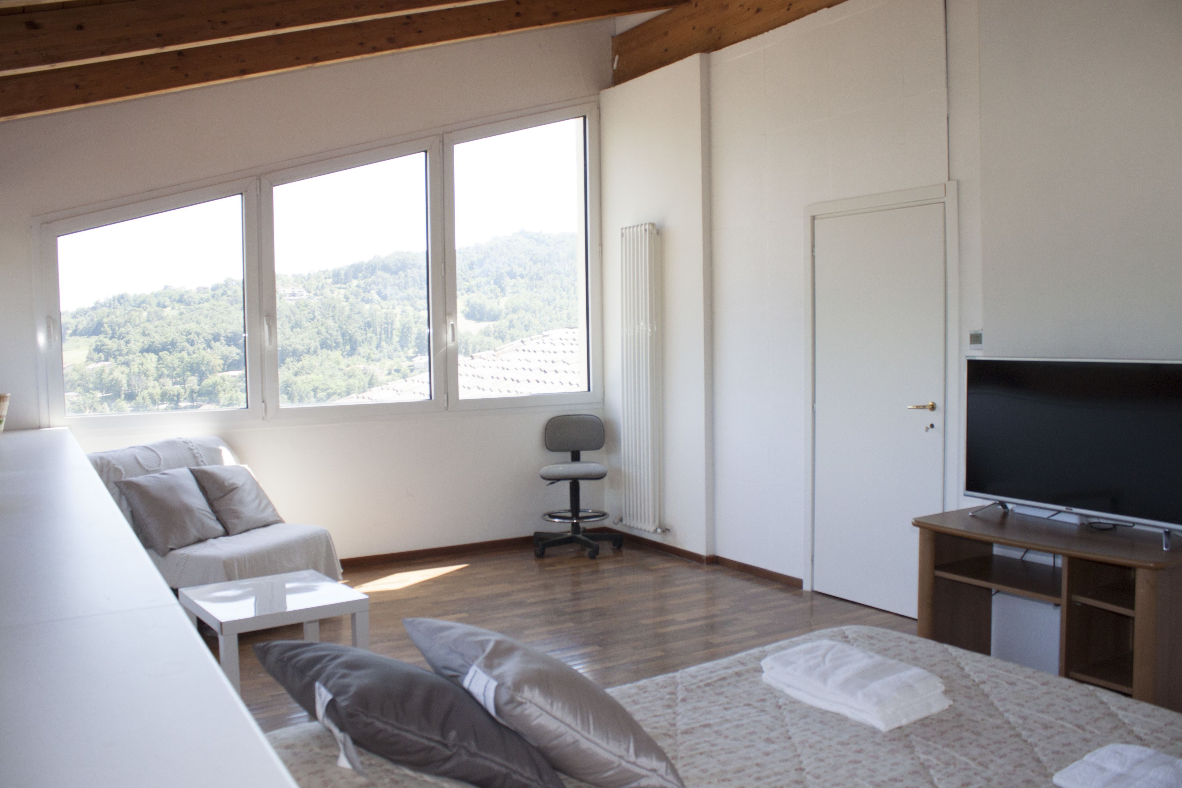 Una habitación moderna y bien iluminada con un ventanal grande, un sofá, un televisor y una mesita.