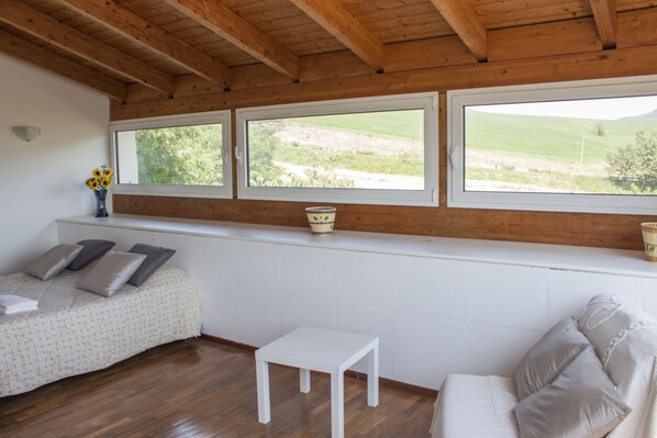 Una habitación con cama, una mesita y una ventana que da a un paisaje verde.