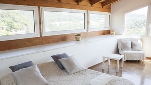 A bedroom with a bed, a small table, a chair, and large windows with a view of greenery. - Casa Bella Il Castello (Vergato)
