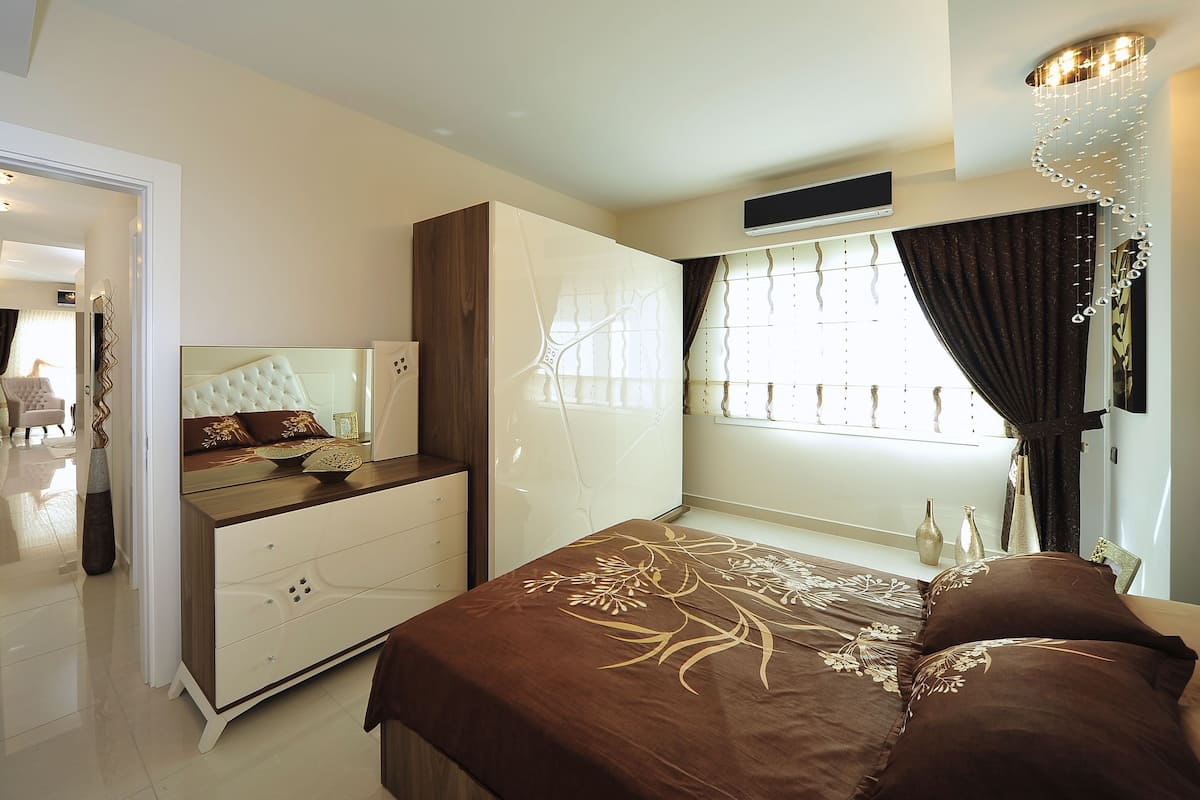 A modern bedroom with a large bed, a dresser, a vanity, and a walk-in closet.