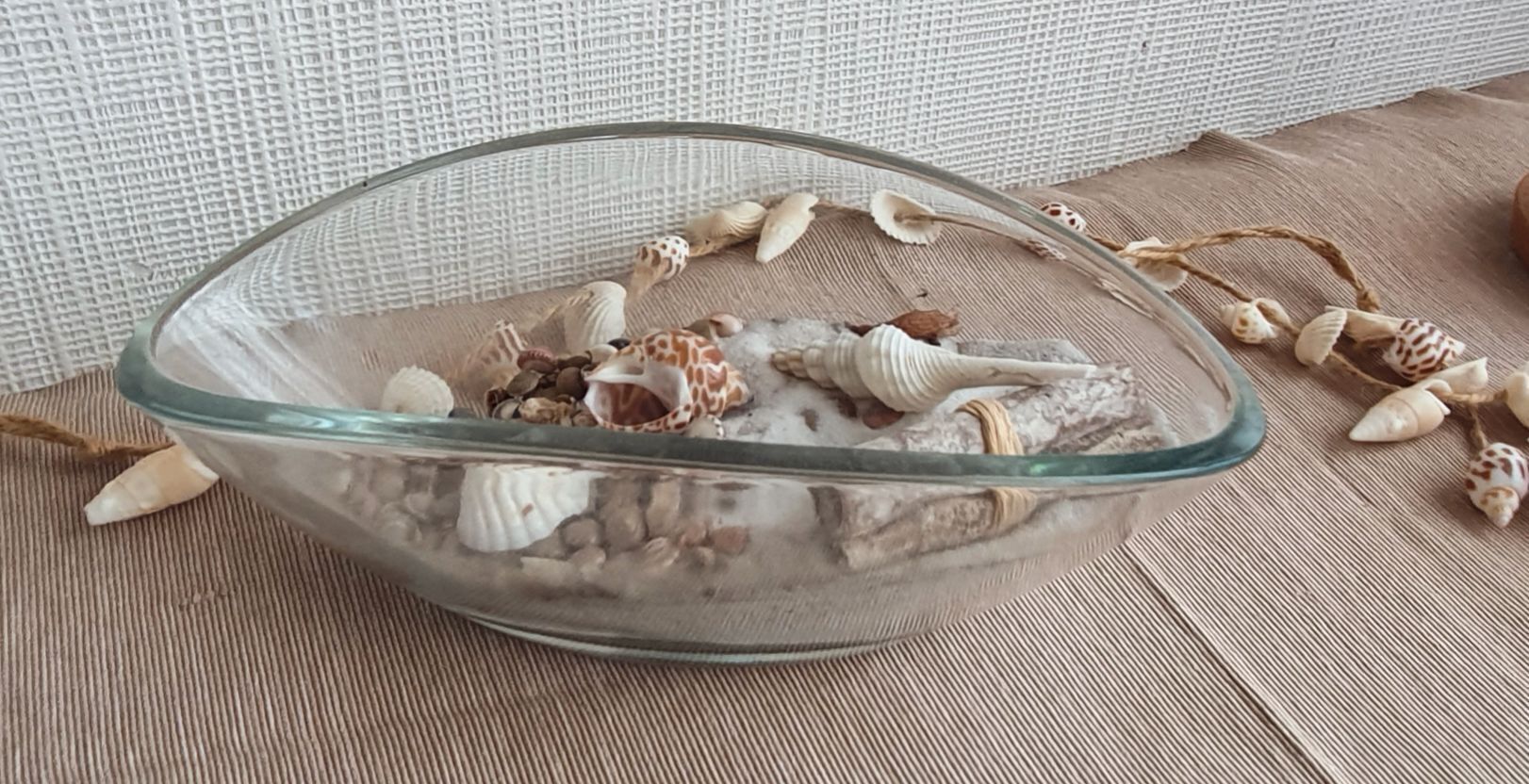 Un bol en verre contenant des coquillages, posé sur une surface en tissu à texture.