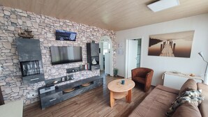 A modern living room with a stone wall, a flat-screen TV, a fireplace, a sofa, and a coffee table. - The cottage in Taddigshörn - nordseereise-net (Esens)