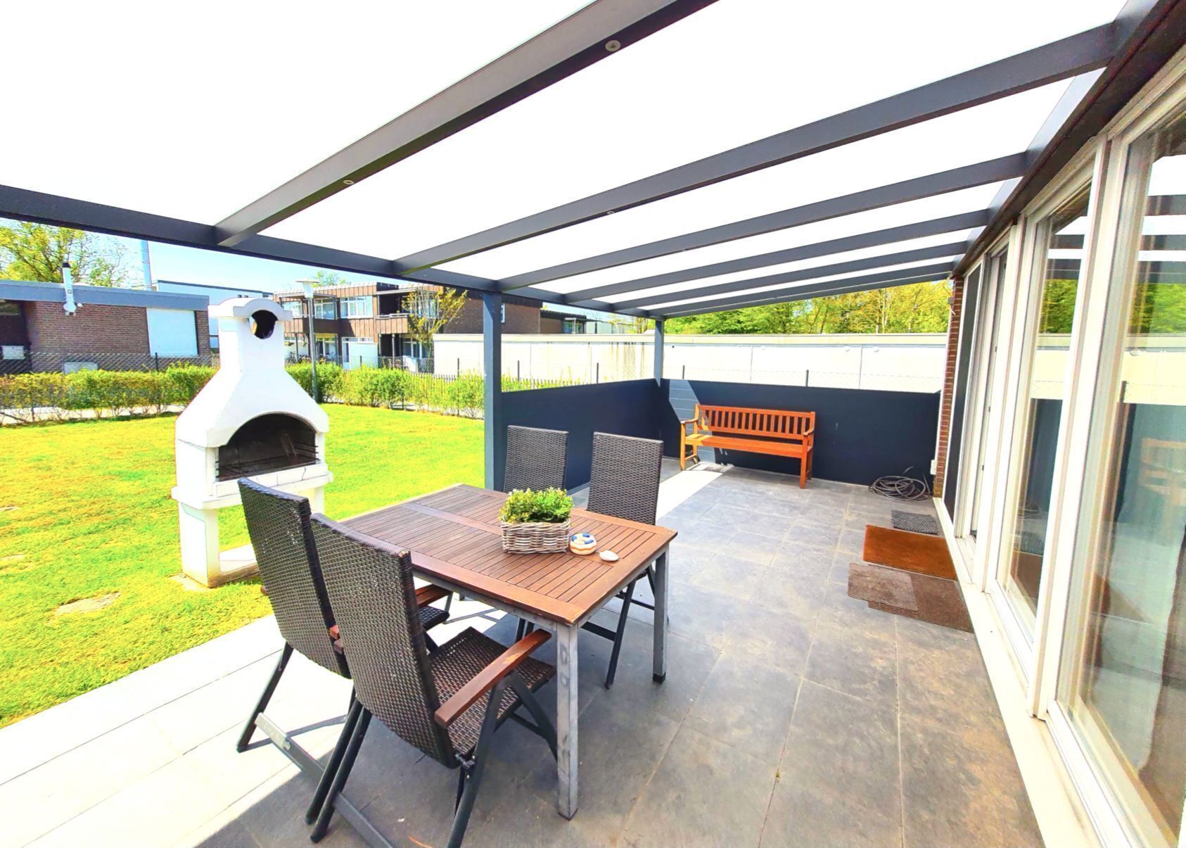 An outdoor patio with a table and chairs, a barbecue grill, and a bench.