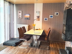 A dining area with a table, chairs, and a vase of flowers. There are pictures on the wall and a fireplace. - The cottage in Taddigshörn - nordseereise-net (Esens)
