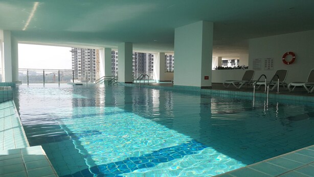 An indoor swimming pool with clear water, tiled floor, and a view of high-rise buildings. - SkyHabitat (Johor Bahru)