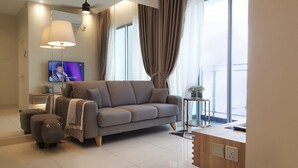 A modern living room with a grey sofa, a small side table with a plant, a TV mounted on the wall, and a large window with curtains. - SkyHabitat (Johor Bahru)