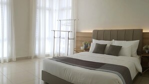 A modern bedroom with a large bed, a wooden headboard, a bedside table with a vase, and sheer curtains. - SkyHabitat (Johor Bahru)