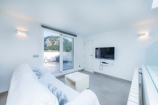 A modern living room with a sofa, a coffee table, a TV, and a sliding glass door leading to an outdoor area.