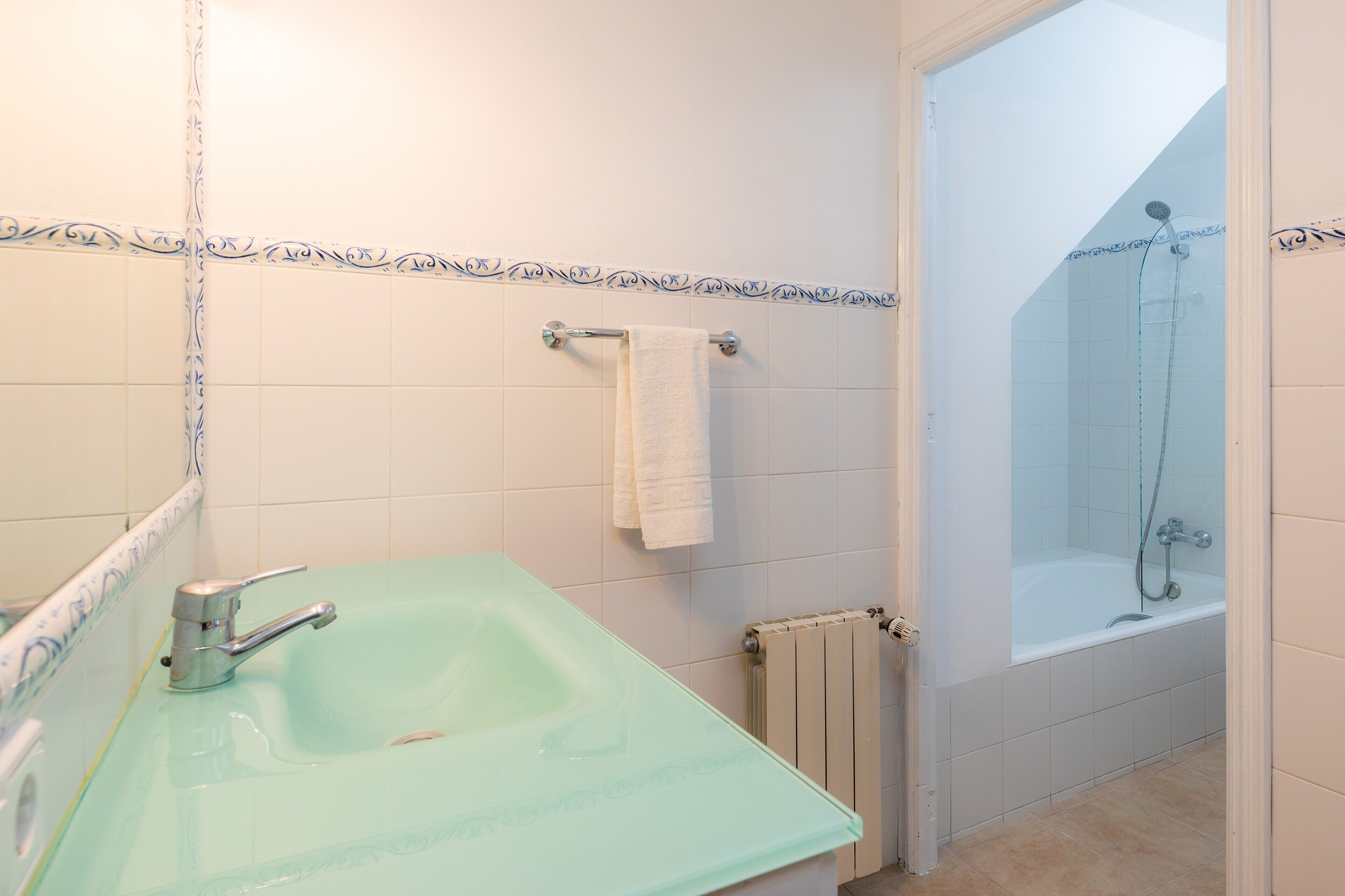 A bathroom with a green sink, a white bathtub, and a towel hanging on the wall.