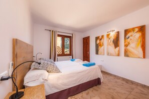A bedroom with a bed, a desk, a chair, a window with curtains, and three paintings on the wall.